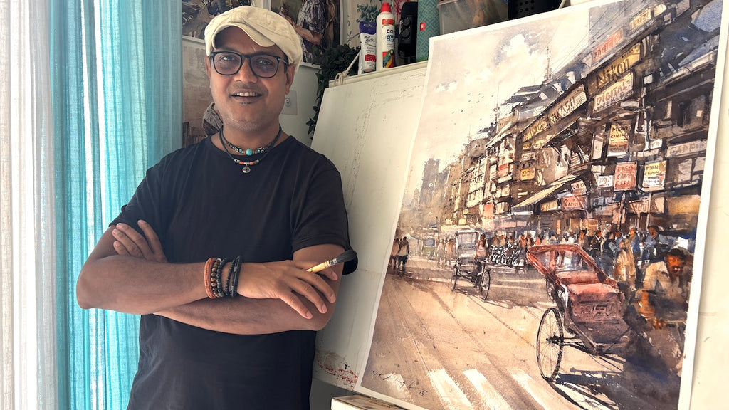 indian watercolor artist Nitin Singh standing next to his cityscape painting.