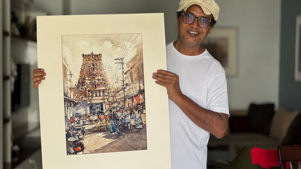 famous watercolour artist Nitin Singh holding a large framed artwork of a bustling street scene.