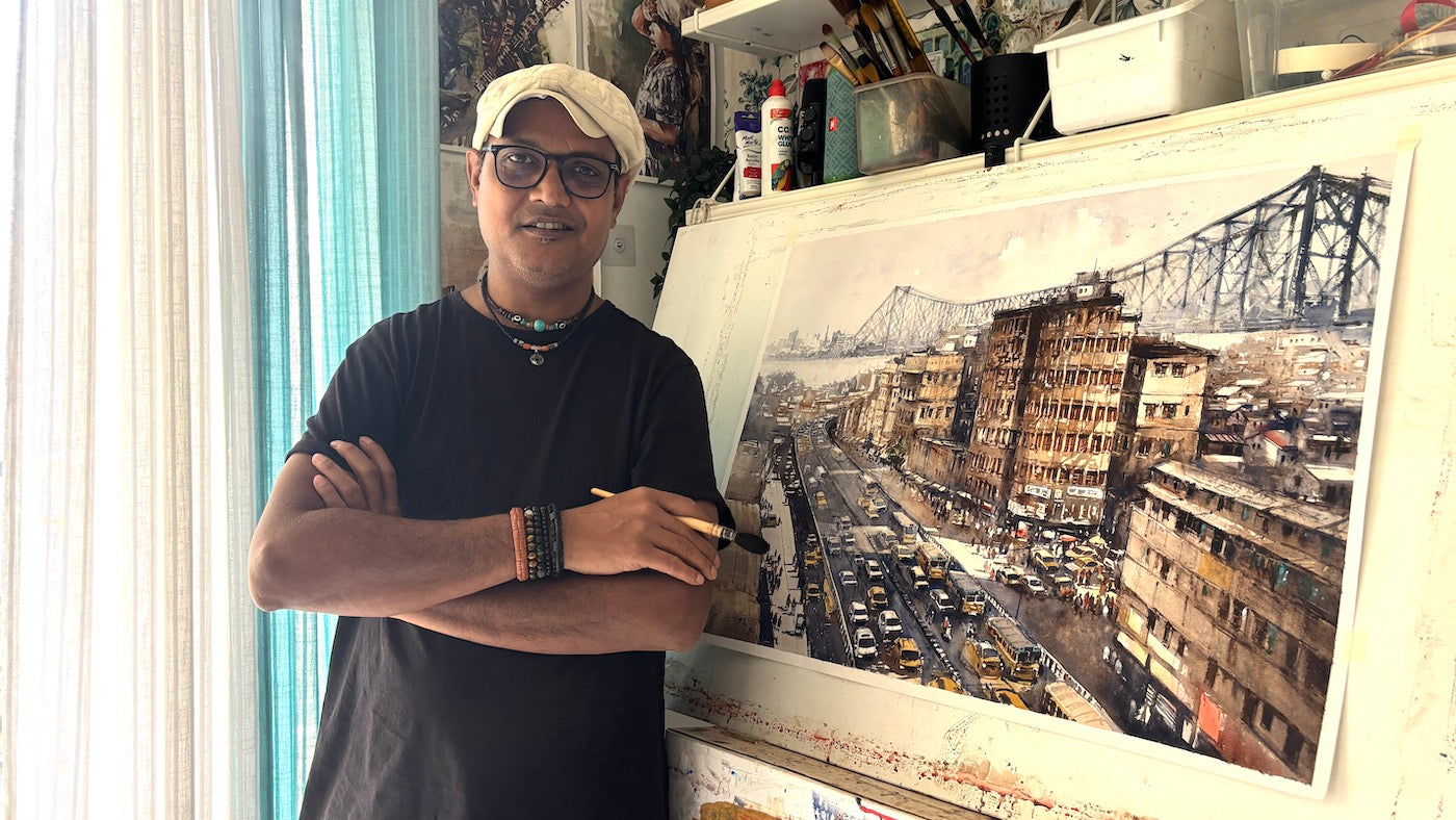 watercolour artist Nitin Singh standing in front of his large kolkota cityscape painting in an art studio.